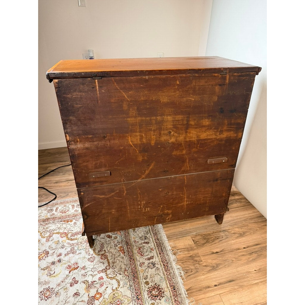 A Late 18th Century New England Pine Two-Drawer Blanket Chest, c. 1780–1810 from Pearl City Antiques, with a timeworn finish and visible scratches and marks, stands on a wood floor near a patterned rug and white wall.