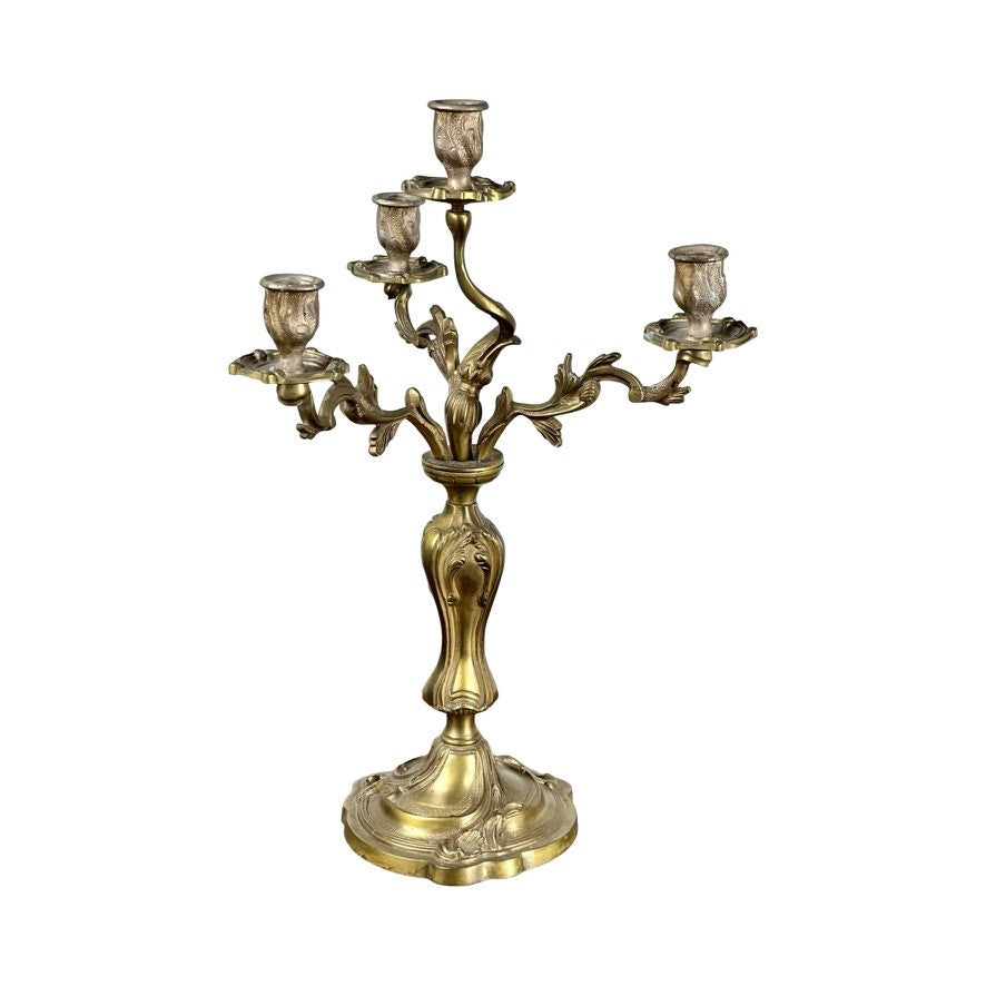 A vintage brass Louis XV style four light candelabra with ornate, curving details stands on a decorated base against a white background. Brand is unknown.