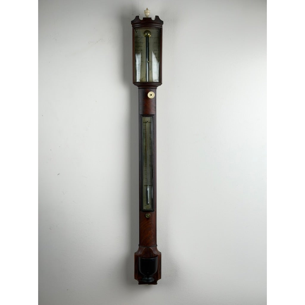 A tall, dark wood English Regency Mahogany Stick Barometer by Thomas Jones, Liverpool, c. 1820, with an upper glass-fronted dial and a thermometer centered on the lower section.