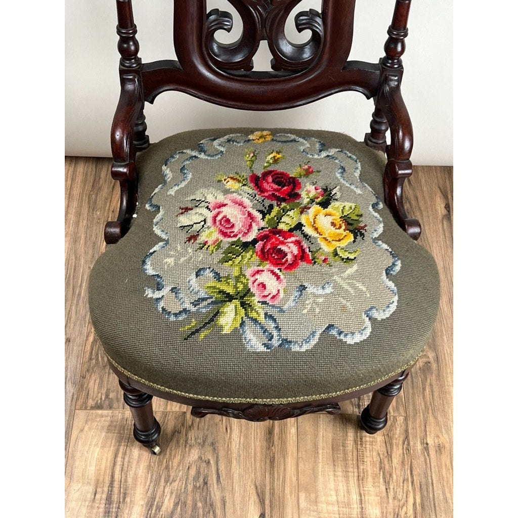 An Antique Victorian Rococo Revival Carved Walnut Slipper Chair (late 19th c.) features a floral needlepoint seat with pink, red, and yellow roses on gray. Brand: None/Unknown. Gracefully set on a wooden floor.
