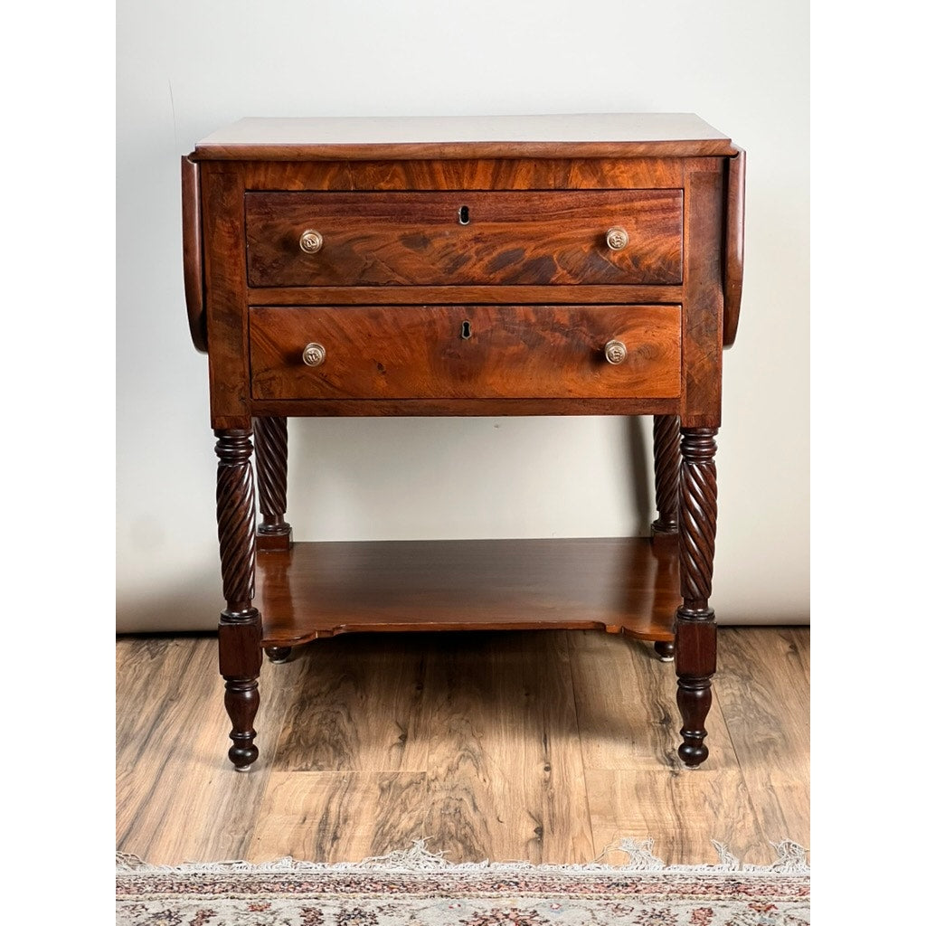 This Antique Federal Mahogany Two Drawer Work Stand c. 1820 features lion's head pulls, twisted carved legs, a lower shelf, and a rich reddish-brown finish evoking antique elegance beside a patterned rug.