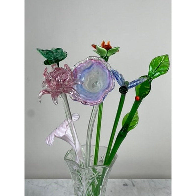 A clear glass vase displays the Vintage Bouquet Murano Art Glass Long Stem Flowers and Butterflies, featuring hand-blown colorful flowers with pink, purple, green, and red petals and leaves against a plain light background.