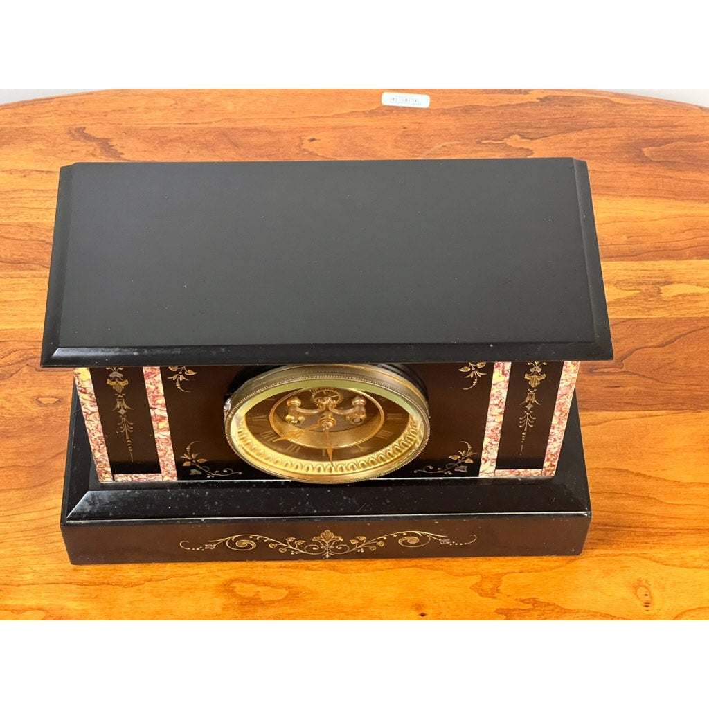 An Antique Victorian Slate Mantle Clock with Open Escapement 8 Day Time and Strike, c. late 19th century, featuring floral inlay and a gold-trimmed round face, sits on a polished wooden surface. Brand: Unknown.