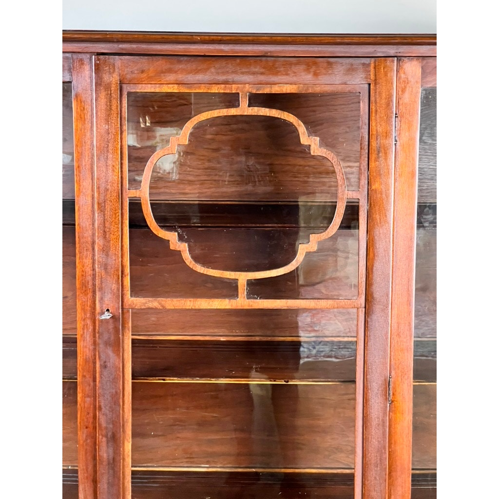 A close-up of a Depression Era Mahogany Curio Display Cabinet with glass doors and sides, circa 1930s, showcasing decorative geometric wooden trim on the glass. The faint reflection of a person on the glass surface further highlights the vintage appeal of this classic American furniture piece. Brand: None/Unknown.