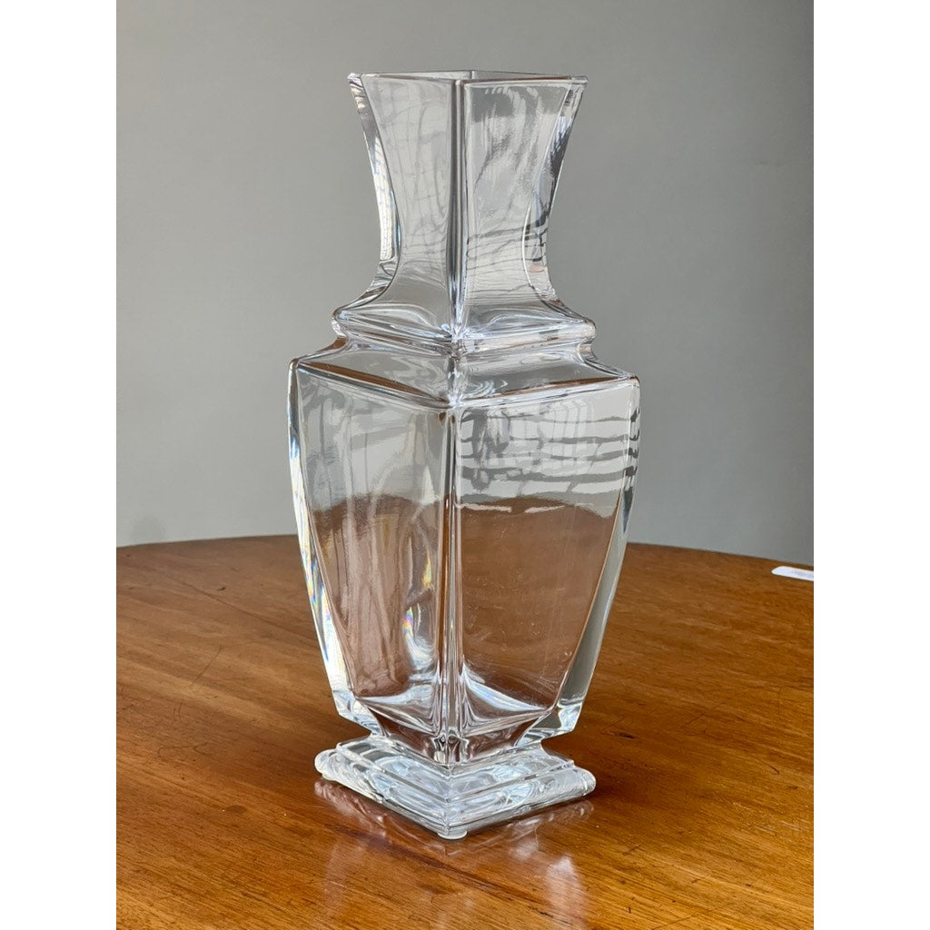 The Vintage Baccarat Crystal Pearl Vase by Baccarat, featuring a geometric design with a square base and flared rim, sits on a wooden surface against a plain gray background.