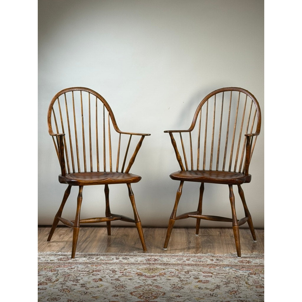 A pair of signed L.E. Partridge Connecticut bench-made continuous-arm Windsor chairs, circa 1960s, sit on a hardwood floor beside a patterned rug and against a plain light-colored wall.