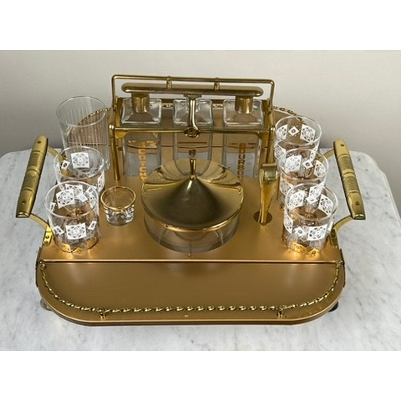 A Vintage Mid Century Modern Bar Caddy (c. 1960s) with ornate handles displays patterned tumblers, a lidded dish, decanters, and a cocktail shaker—all neatly arranged on its marble surface. Brand: Unknown.