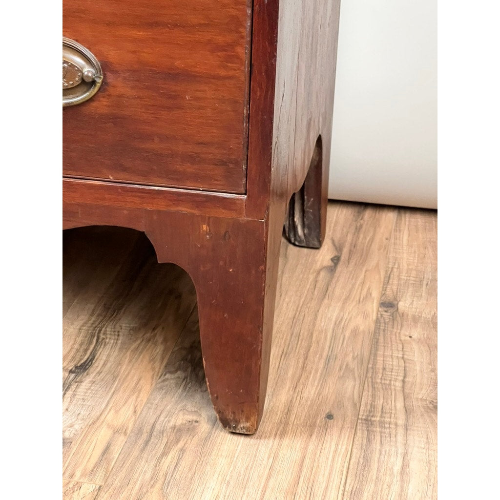 Close-up of the lower corner of a Rare Labeled William Lloyd Springfield, Massachusetts Federal Cherry Chest of Drawers, circa 1800, showing its early American-style brass handle, legs, and some wear on the finish as it stands on a light wood floor.
