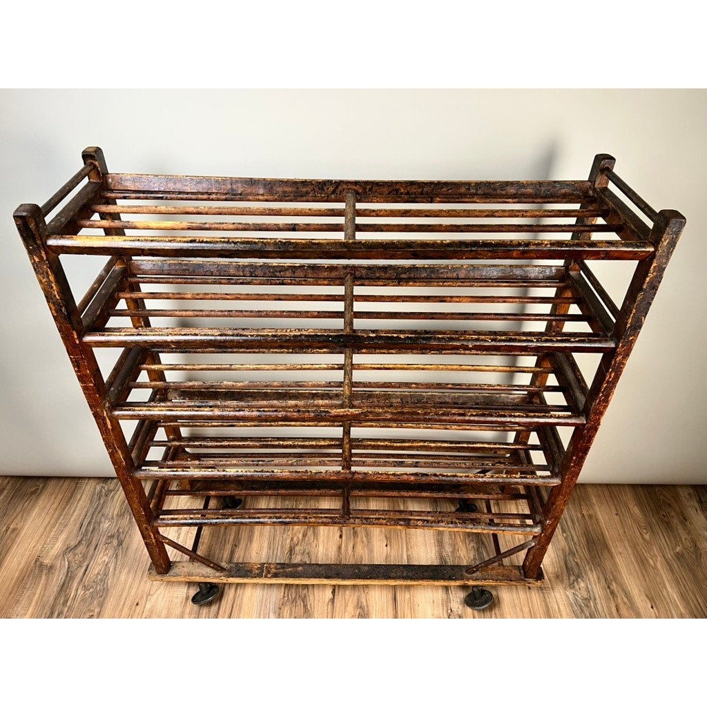 The Antique Oak Shoe Factory Rolling Rack on original industrial casters (late 19th c.) features multiple horizontal shelves and a rustic, worn finish, perfect for storage or display against any wall. Brand: None/Unknown.