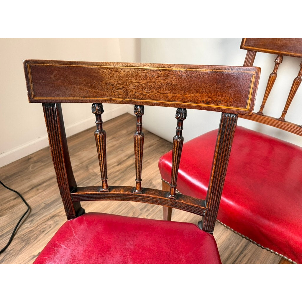 Two neoclassical dining chairs from the Assembled Set of Six English George III Mahogany Neoclassical Dining Chairs by Pearl City Antiques, featuring intricate spindle backs and bright red cushioned seats, are placed on a wood floor. One chair is fully visible, while part of a second chair can be seen in the background.