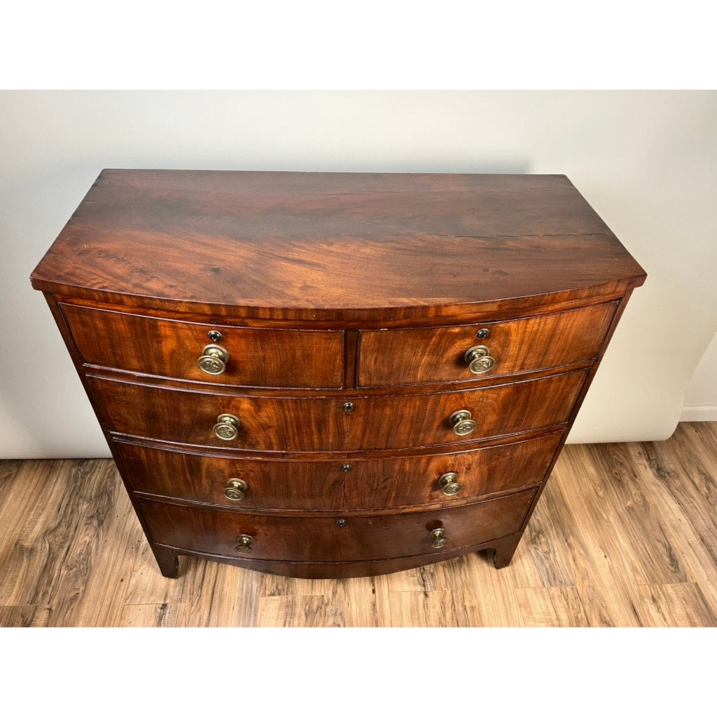 An Antique George III Mahogany Bowfront Chest on French Feet, c. Late 18th Century, features four drawers with brass handles and stands on a wood floor against a plain white wall. Brand: Unknown.