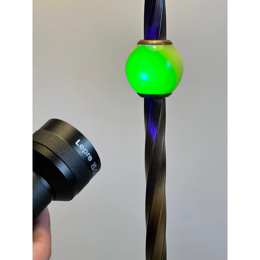 A hand holds an Antique Art Deco Uranium and Slag Glass Lamp c. 1920, its glowing green orb atop a twisted staff reminiscent of an old floor lamp, illuminated against a plain background.