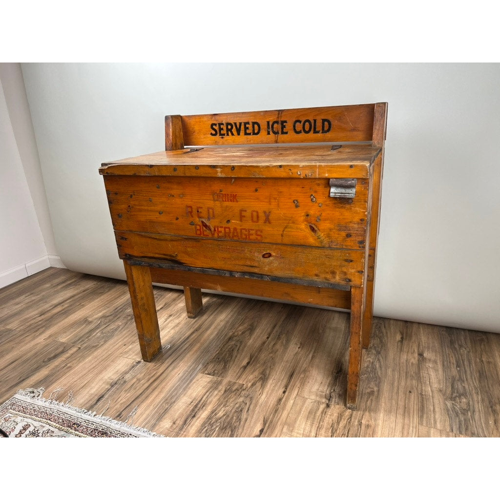 An Antique Tin Lined Pine General Store Red Fox Ginger Ale of Rhode Island Cooler c. 1930 stands on legs against a light wall and wood floor—a vintage Red Fox soda cooler evoking the charm of early general stores.