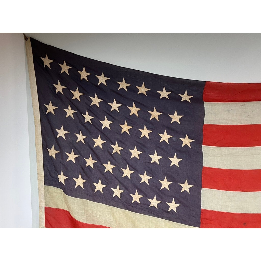An Antique 45 Star American Flag from the Spanish–American War era (9’9 x 6) with classic red, white, and blue fabric hangs against a plain white wall. Its gently worn appearance reflects historic Americana. Brand: None/Unknown.