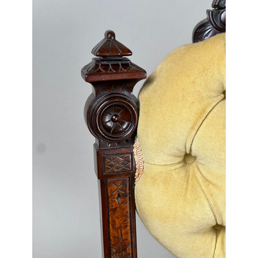 Close-up of a finely carved walnut chair arm with intricate Renaissance Revival motifs beside a tufted light yellow cushion—detail from an antique pair of side chairs attributed to John Jelliff, Newark, c. 1880.