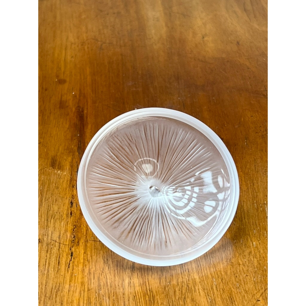 The Vintage Lalique France Ballerina Frosted Crystal Covered Powder Box by Lalique sits on a wooden surface, its decorative lid casting bright curved reflections on the right.