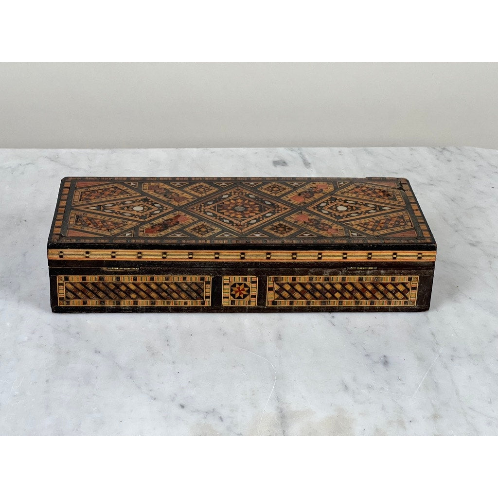 An Antique Persian (likely Syrian) Khatam Inlaid Wood Jewelry Box, early 20th century, with intricate geometric marquetry in brown, gold, and black, is displayed elegantly on a white marble surface.