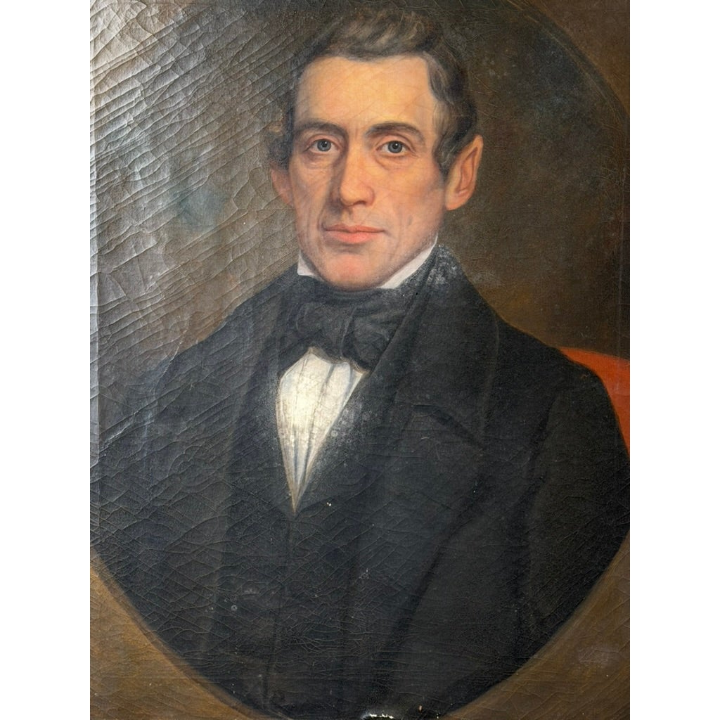 An antique oil portrait of a 19th-century man wearing a dark coat and black necktie, presented within an oval frame, from the Pair of American School Oil Portraits of a Gentleman and Lady, c. 1840–1860 by Pearl City Antiques.