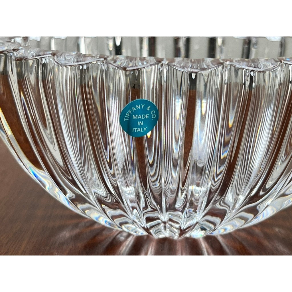 A close-up of a Vintage Tiffany & Co Crystal Bowl in a ribbed petal design with a blue "Tiffany & Co. Made in Italy" sticker, placed on a wooden surface.