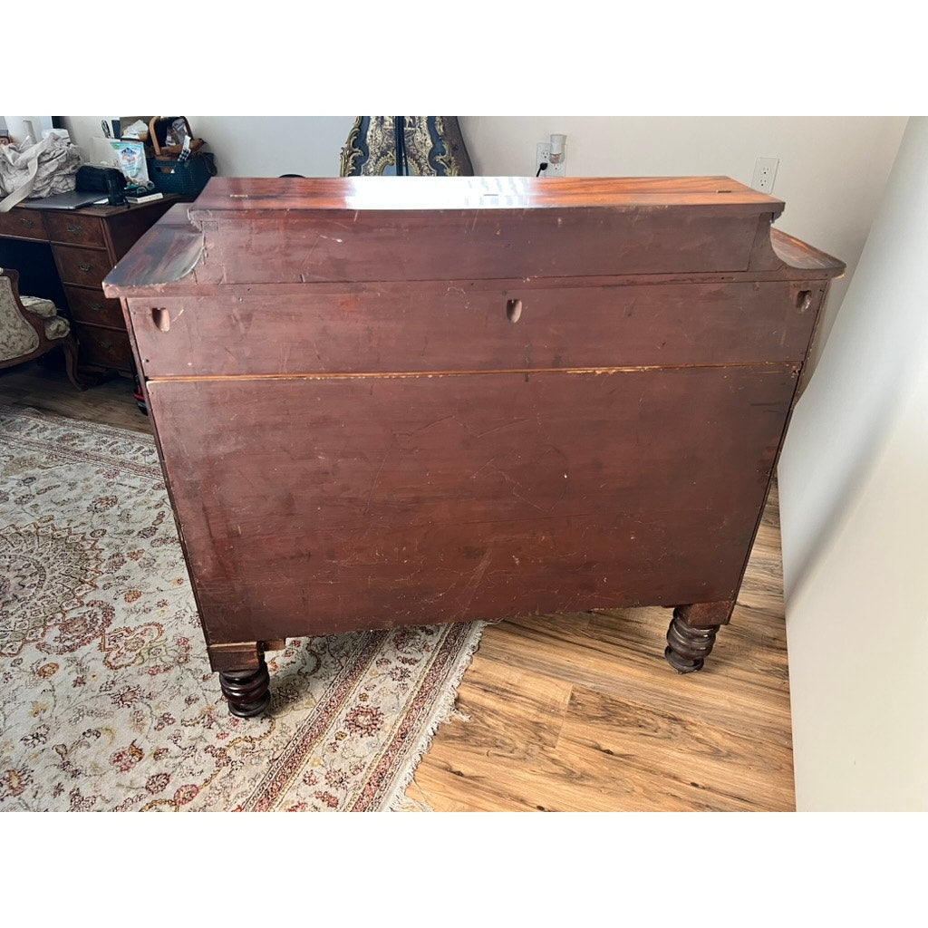 An Antique American Empire Albany Four Drawer Chest c. 1840 stands on a hardwood floor beside a patterned rug and other furniture in a sunlit room.
