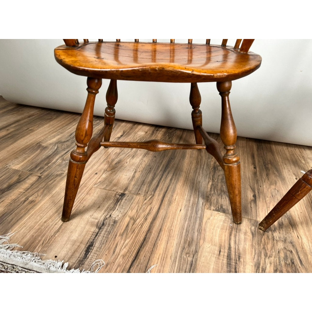 Close-up of an Antique Near Pair 18th Century Windsor Chair with spindle legs and curved seat on a wood-patterned floor; part of a rug appears in the lower left. Brand: None/Unknown.