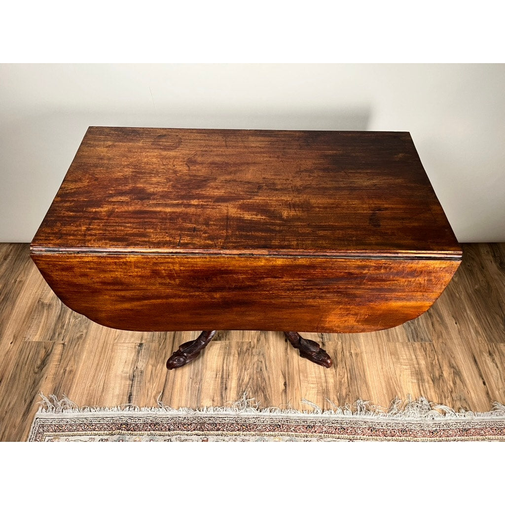 A top-down view of an Antique American Empire Drop Leaf Table with Great Eagle Carved Feet c. 1840 sits on a wooden floor, partially over a patterned rug. The table has a rich brown finish and is placed against a plain white wall. Brand: None/Unknown.