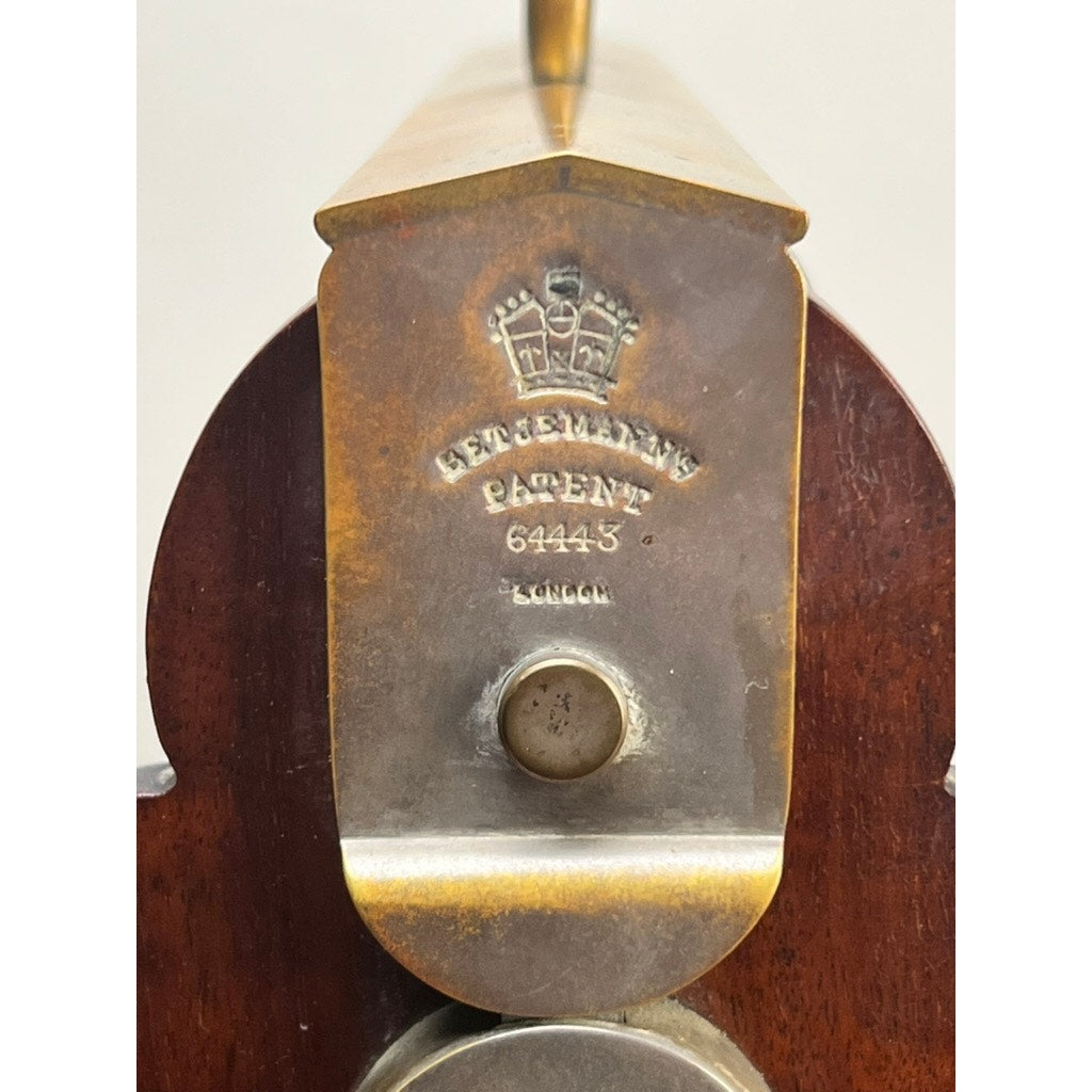 Close-up of a metal plate engraved with a crown and “Gesteins Patent 64445 London” on an Antique English Edwardian Betjemann’s Cut Crystal Three Bottle Tantalus (early 20th century) by Betjemann's, attached to the wooden end.
