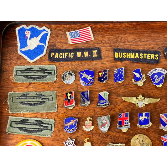 A striking World War II grouping from Pearl City Antiques, the Attributed WWII 158th Infantry Bushmasters Grouping of Frank W. Slatcher, Company I, Pacific Theater, featuring a collection of military patches and pins—including Pacific W.W. II memorabilia from the storied 158th Infantry Regiment—displayed with a U.S. flag and assorted insignias and badges that honor historic service.