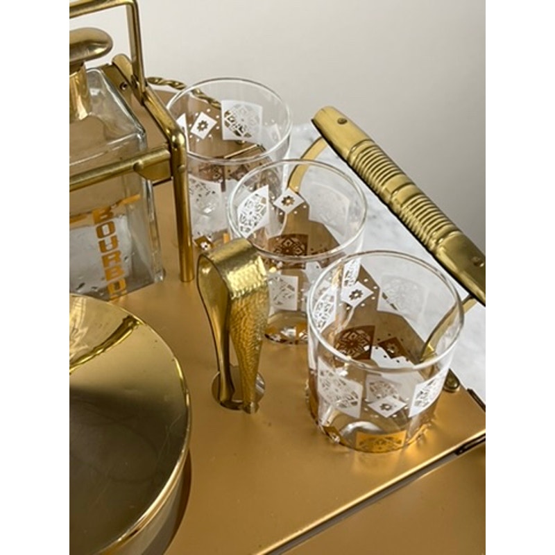 A close-up of the Vintage Mid Century Modern Bar Caddy c. 1960s displays a gold-handled stirring spoon, three patterned glasses with amber liquid, and a square Bourbon-labeled decanter. Brand: None/Unknown.