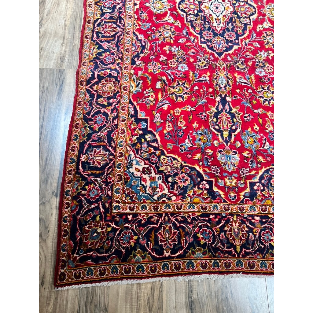 A close-up of a Vintage Hand-Knotted Persian Kashan Wool Gallery Rug (c. 1950–1970, 4’5 x 8’8) with intricate blue, gold, and cream floral patterns and a detailed border, displayed on a wooden floor. Brand: None/Unknown.