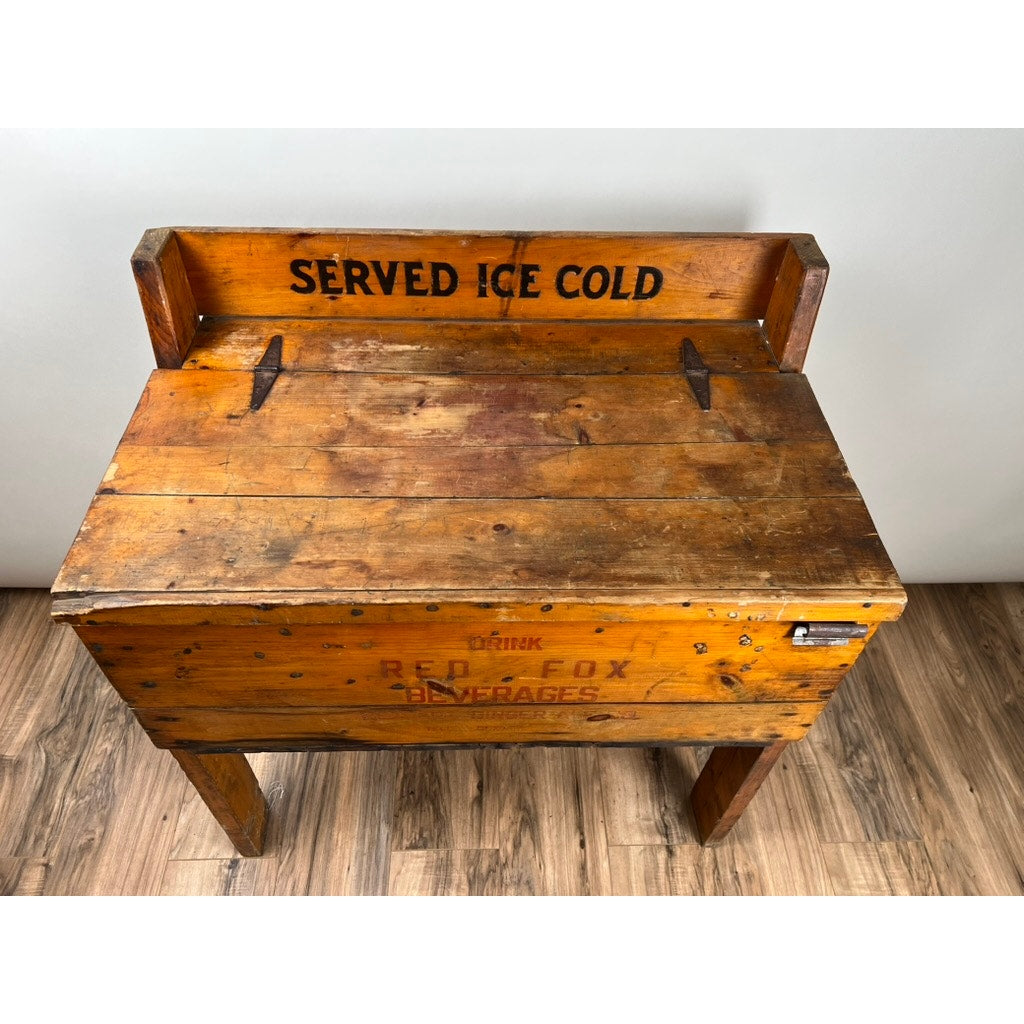 An Antique Tin Lined Pine General Store Red Fox Ginger Ale of Rhode Island Cooler c. 1930, with SERVED ICE COLD on the backrest and faint RED FOX on the front, evokes a classic early-1900s general store scene.