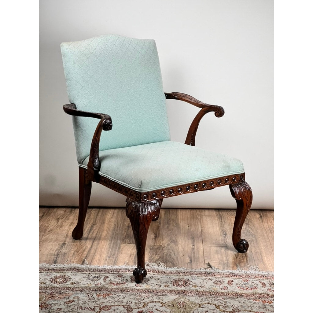 An Antique George II Mahogany Gainsborough Open Arm Chair (mid-19th century) with a carved frame and cabriole legs, upholstered in light blue patterned fabric, sits on a wood floor with part of a patterned rug visible beneath.