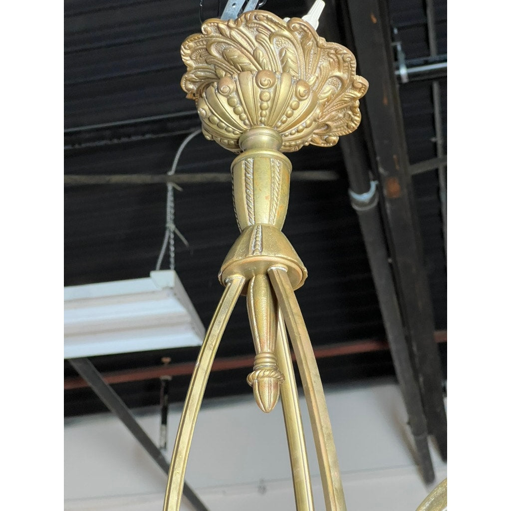 Close-up of a Vintage Muller Frères Lunéville French Brass and Art Glass Four Light Chandelier, featuring ornate leaf and bead detailing, suspended from a dark ceiling with visible pipes and wires in the background.