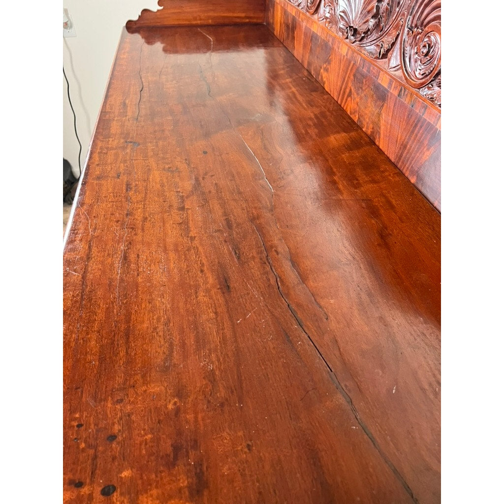 Close-up of an Antique American Empire Mahogany Sideboard, probably Philadelphia c.1840, showing polished surface with visible grain and light scratches; rosewood edge banding features ornate carved design. Brand unknown.