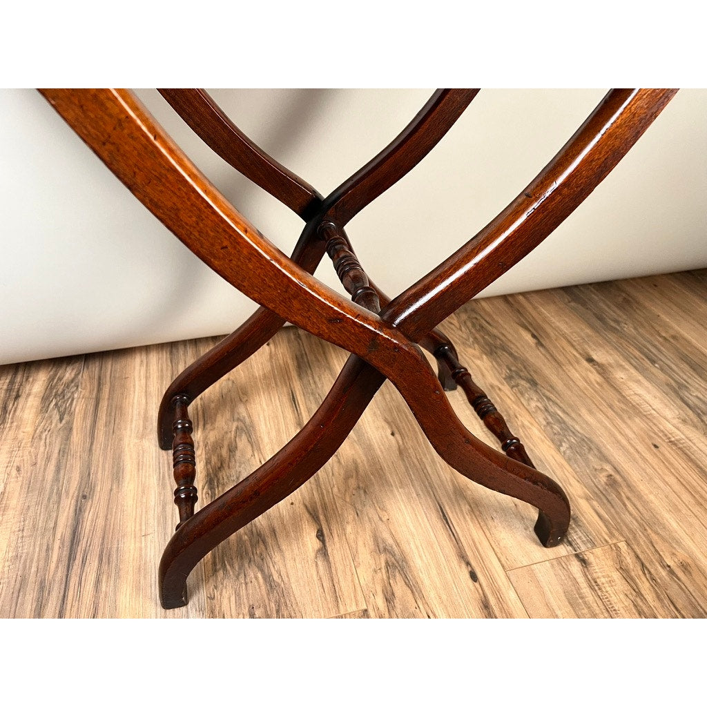 Close-up of the crossed wooden legs of an Antique English Regency Mahogany Folding Coaching Table (c. 1825–1845), set on a light wood floor. The polished, turned legs highlight its classic vintage style. Brand: None/Unknown.