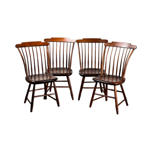 A set of four JR Hunt antique New Hampshire step down Windsor chairs—early 19th century, signed—features high spindle backs, angled legs, and a dark brown finish, echoing classic American style against a white background.