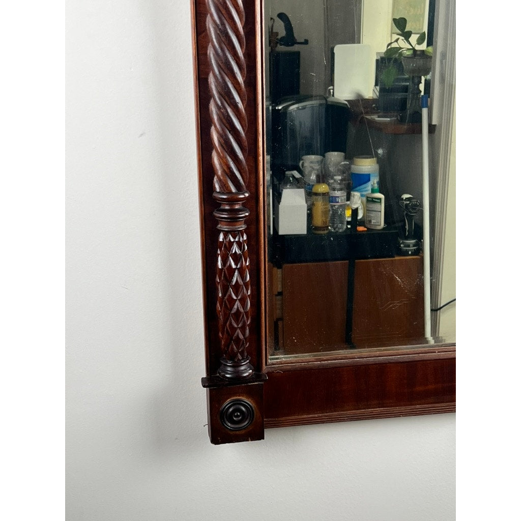 An Antique American Empire Mahogany Pier Mirror c. 1840 reflects a countertop with bottles, containers, and a sink; the photo focuses on the left side of this intricately carved antique mirror and its frame. Brand: None/Unknown.
