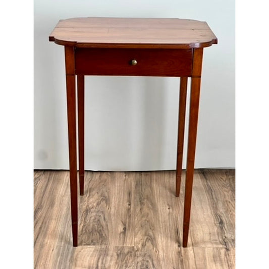 A Fine Antique Federal Period Cherry One Drawer Hepplewhite Stand, c. 1820 by Pearl City Antiques, featuring a single drawer and slender legs, is placed on a wood-patterned floor against a plain white wall.