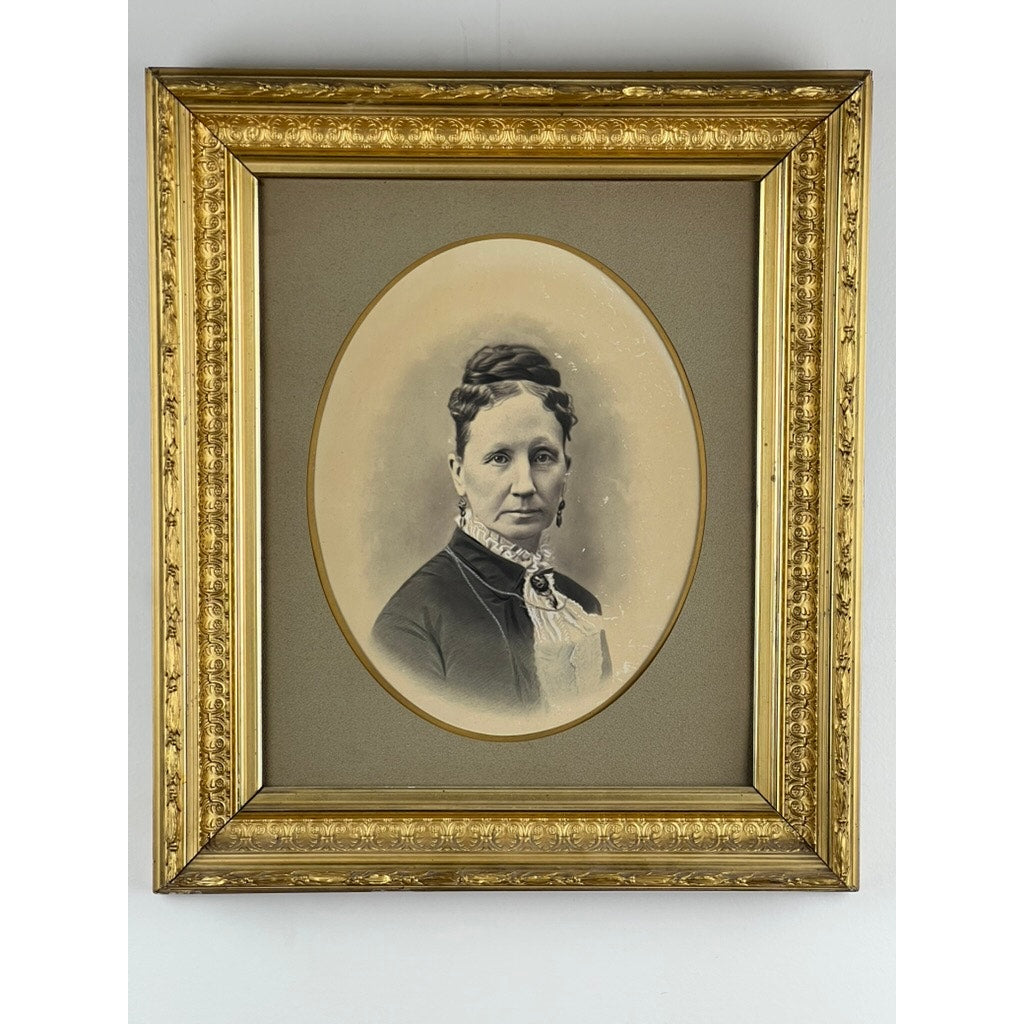An Antique Civil War Era Portrait of a Woman in a gilt wood frame, featuring a sepia-toned oval image with her hair pinned up and dressed in Victorian attire, displayed on a wall. Brand: Unknown.
