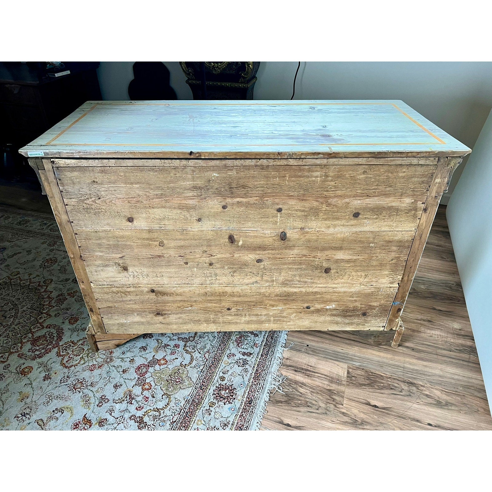 An Antique Italian Paint Decorated Four Drawer Commode c. Early 19th Century with a flat, light-colored top and visible wood grain stands by a patterned carpet and white wall, capturing Italian provincial charm.