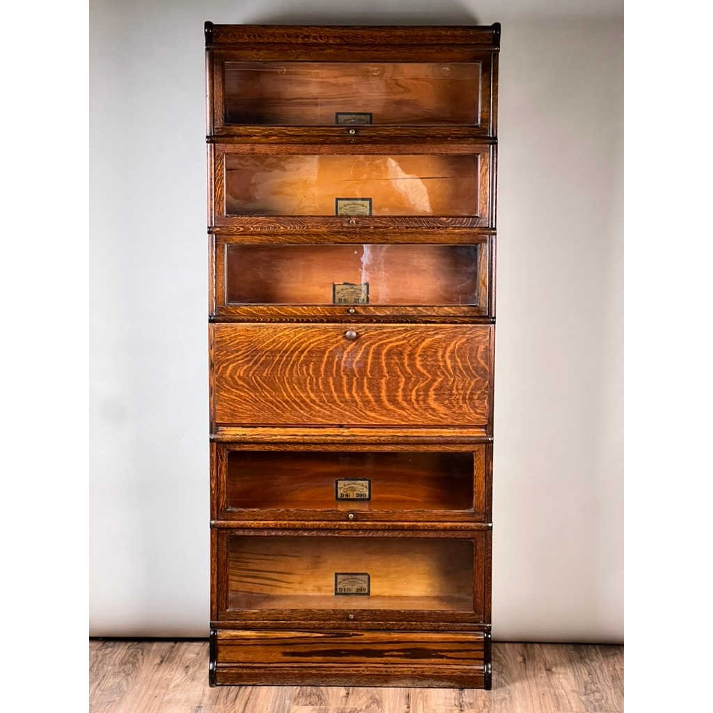 The Antique Globe-Wernicke Quarter Sawn Oak 6-Stack Barrister Bookcase Secretary Desk (c. 1905–1915) by Globe Wernicke, crafted from quarter-sawn oak with six stacked sections featuring glass-front doors and label holders, stands on a wood floor against a plain light background.