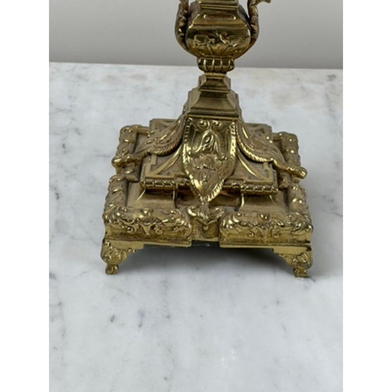 This Antique Pair of Late 19th Century Brass Three Light Candelabra features an ornate gold-toned metal base with intricate scrollwork, leaf motifs, and raised patterns, making it a striking example of Victorian decorative style.