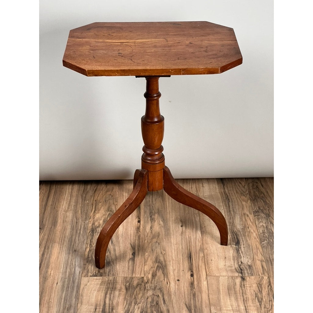 An Antique 19th Century Cut Corner Hepplewhite Candle Stand featuring an octagonal top, turned pedestal, and three curved legs stands on a wood-patterned floor against a plain white background. Brand: None/Unknown.