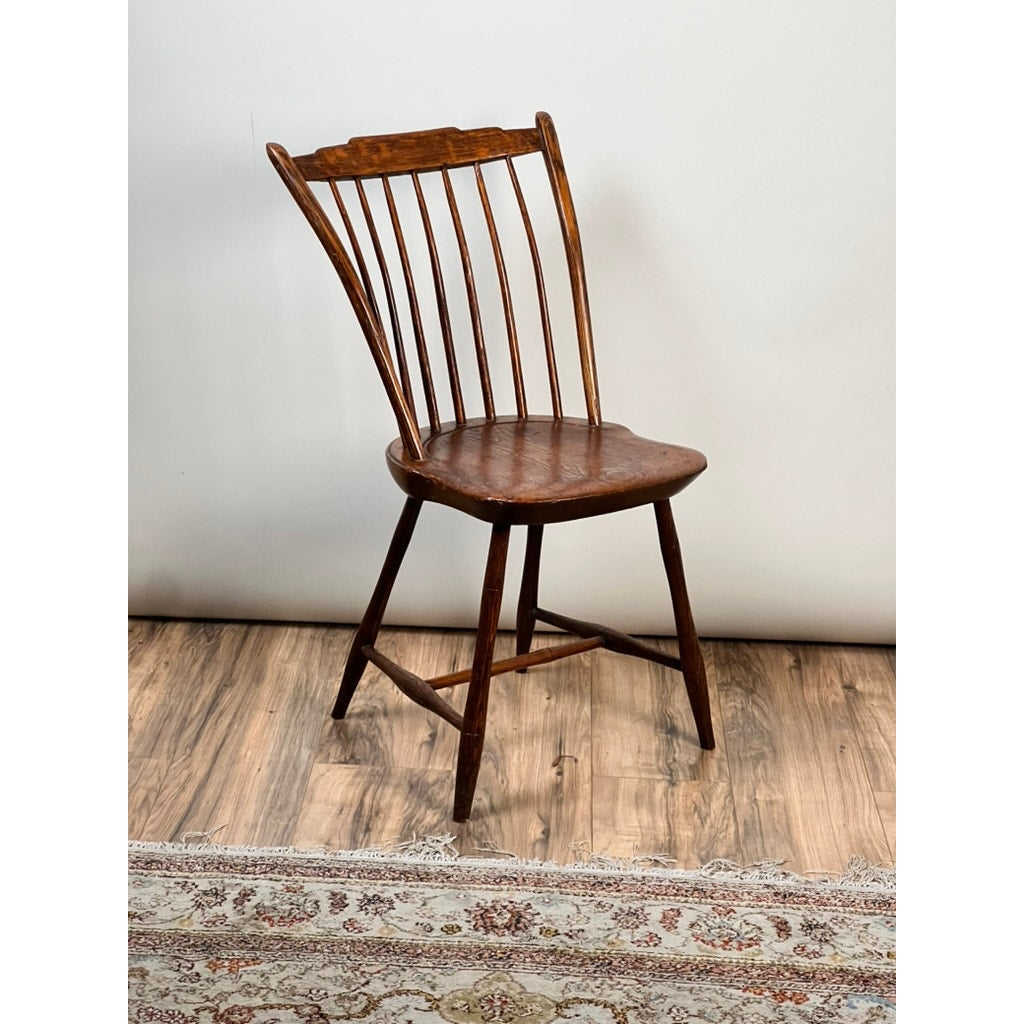 An Antique Step Down Windsor Chair in Oak and Pine, c. Early 19th Century, sits on a wooden floor near a patterned rug against a plain white wall.