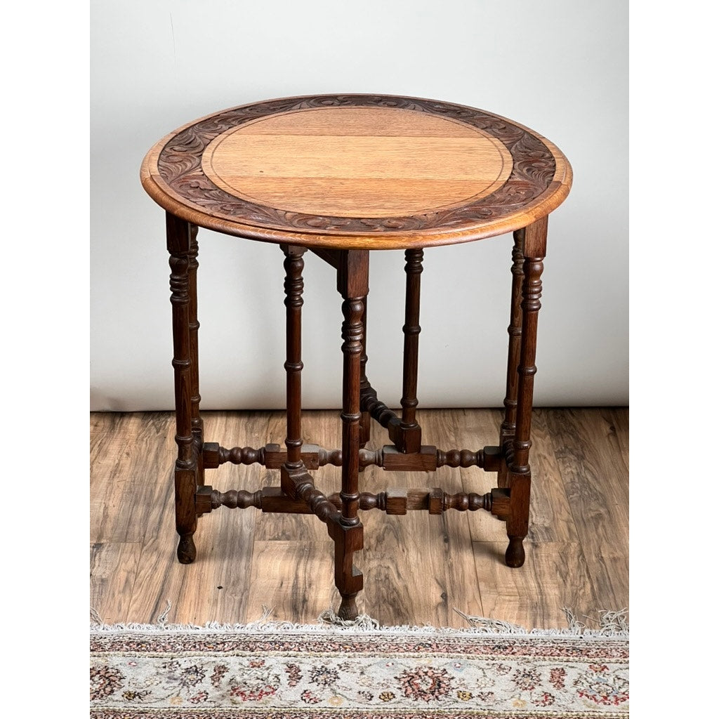 The Antique English Oak Carved Gateleg Occasional Table, c. Late 19th Century, features ornate carved edges, six turned legs joined by decorative stretchers, and stands on a wood floor with a patterned rug—evoking timeless elegance.