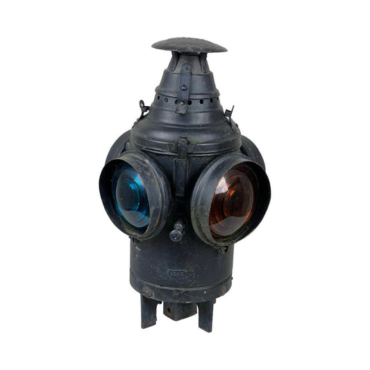 The Antique Illinois Central Railroad Signal Lantern by Dressel features a worn black metal body, vented conical top, and four round lenses—two red and two blue—mounted on the sides, highlighting its vintage, aged appeal.