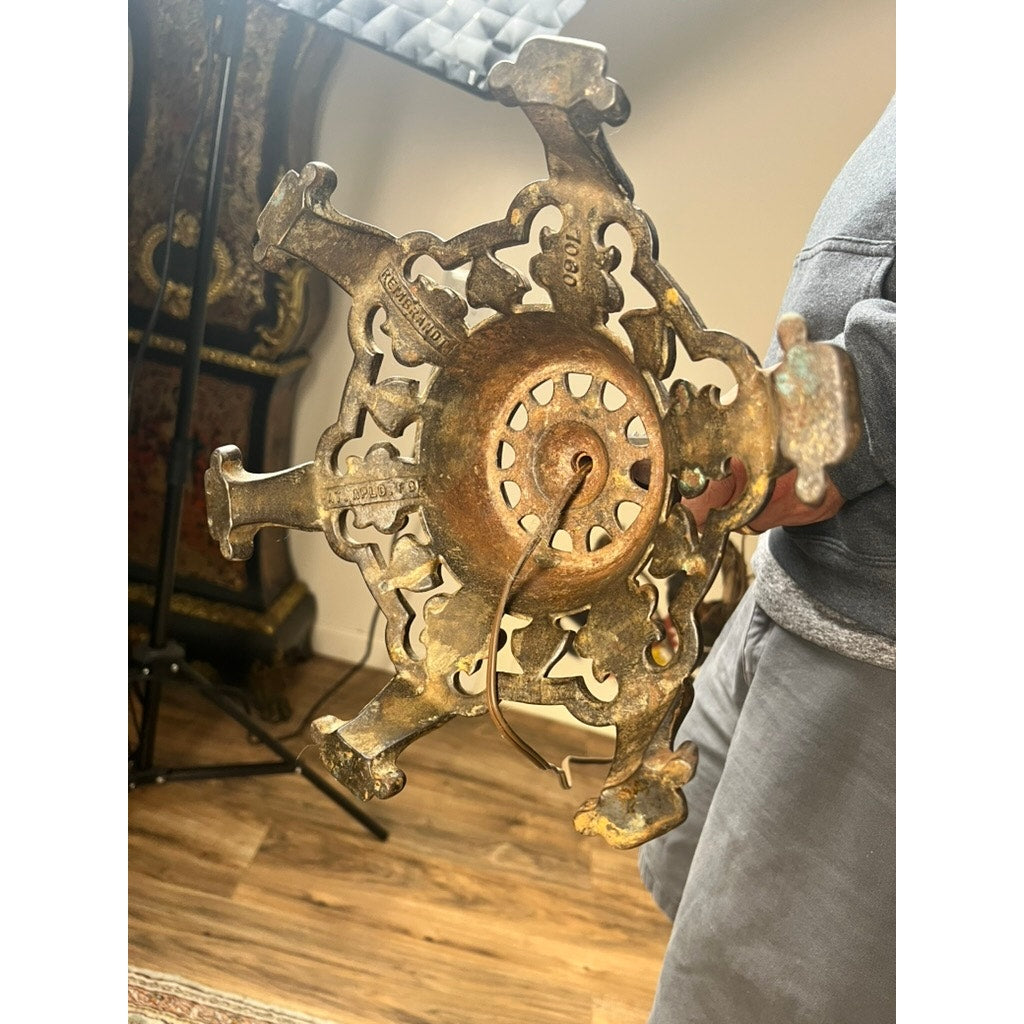 A person holds an Antique Art Deco Cast Iron Floor Lamp base by Rembrandt, featuring ornate cut-out designs and a central circular area, against a wooden floor background.