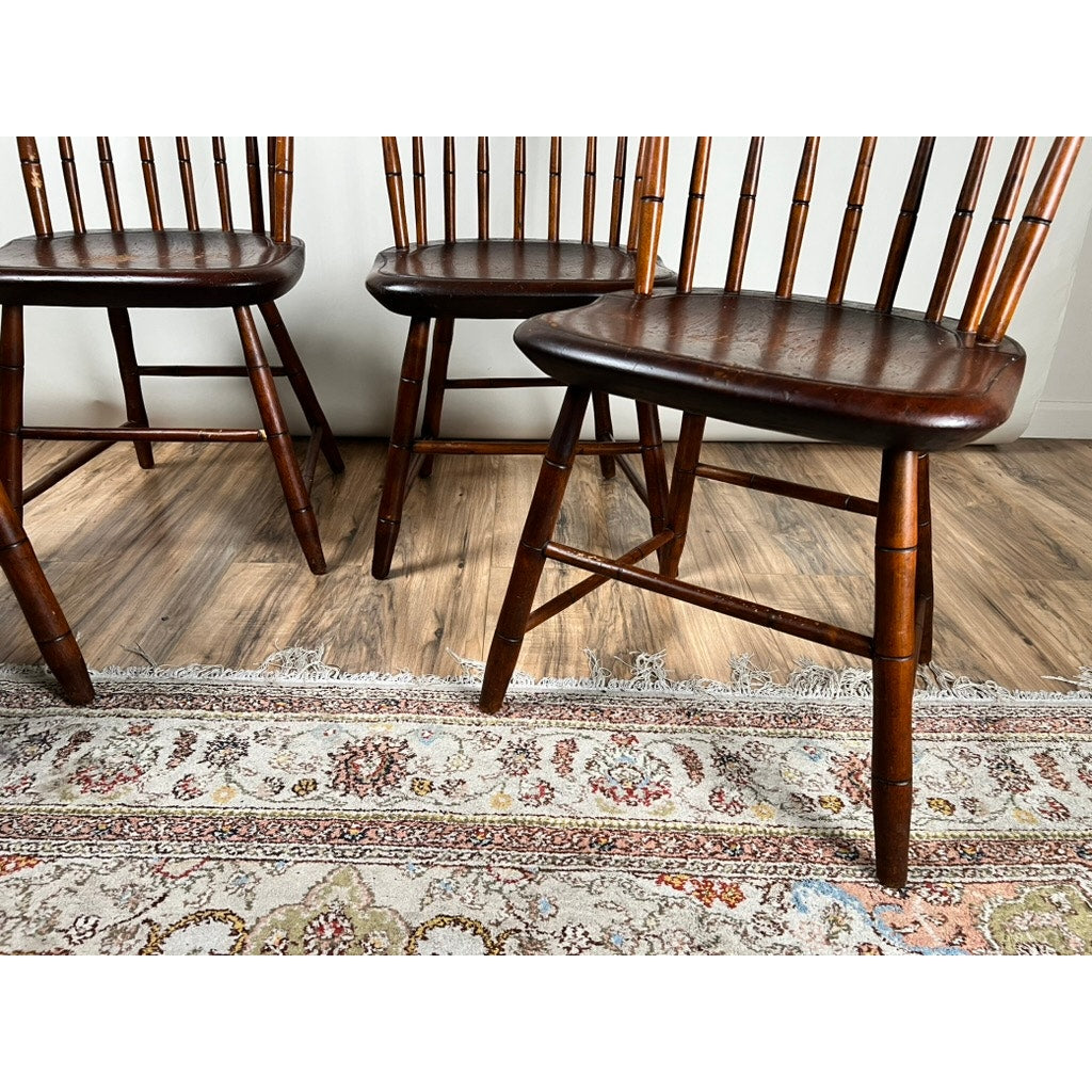 Four JR Hunt Antique Step Down Windsor Chairs (early 19th century) with dark brown finishes and rounded seats sit on a light wood floor beside a floral rug, their lower and middle portions visible.