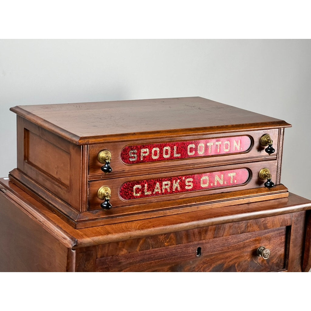 This Antique Victorian Pine Two Drawer Clark’s O.N.T Spool Cabinet by Clark's ONT, c. late 19th century, features red “SPOOL COTTON” and “CLARK’S O.N.T.” labels plus brass and black knobs. A classic wooden piece for vintage decor.
