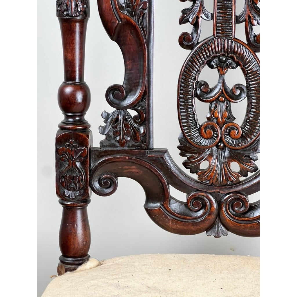 Close-up of antique fine carved Flemish side chair (attributed to Daniel Marot, late 17th century) shows an ornate Baroque chair back with intricate floral and scroll motifs, beige cushioned seat, and a turned leg. Brand unknown.